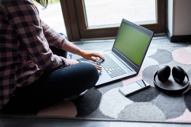 Serbest çalışan bir kadın dizüstü bilgisayarda oturuyor, büyük pencerelerin yanında yerde oturuyor, içeriği olan bir kadın not defterine bakıyor, çalışıyor, evden çalışıyor..