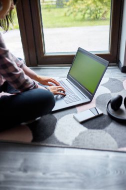 Serbest çalışan bir kadın dizüstü bilgisayarda oturuyor, büyük pencerelerin yanında yerde oturuyor, içeriği olan bir kadın not defterine bakıyor, çalışıyor, evden çalışıyor..