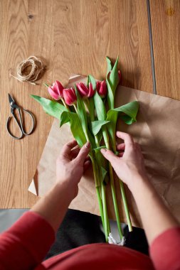 Ahşap masa üzerinde pembe lale buketi düzenleyen kadın elleri, çiçeklerle dolu iş yeri, iş yeri, diy, bahar hediyesi konsepti yukarıdan.
