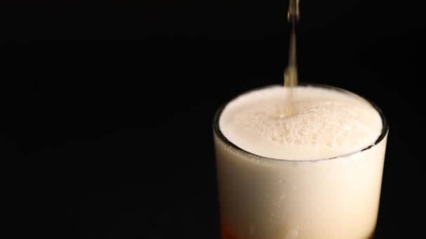 Закрыть наливая пиво с пузырьками и пеной в стекло на черном фоне — стоковое видео