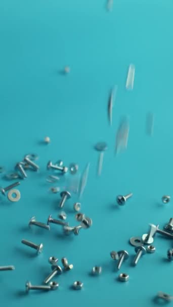 Вертикальное видео Металлический винт, гайки и болты, падающие на синий фон — стоковое видео