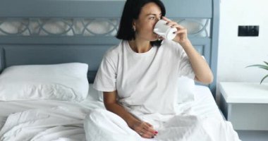Woman having breakfast in bed with coffee or tea cup in bedroom at home, Morning rituals. Breakfast in bed, cozy hotel room.