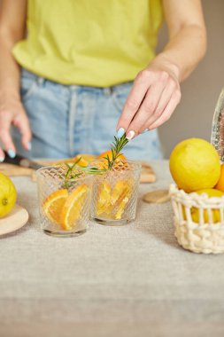 Kadın eli biberiyeyi bardağa, hazırlayan kadın turunçgil ve biberiyeli taze limonatayı evdeki beyaz bir masada, yaz içeceği, sağlıklı su detoksunda yapıyor..
