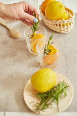 Kadın eli biberiyeyi bardağa, hazırlayan kadın turunçgil ve biberiyeli taze limonatayı evdeki beyaz bir masada, yaz içeceği, sağlıklı su detoksunda yapıyor..