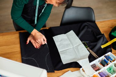 Tepeden tırnağa kadın terzinin dikiş kalıpları atölye, tekstil endüstrisi, hobi ve çalışma alanında dikiş desenleriyle çalışan olgun bir terzi. Oluşturma süreci DIY, Terzinin İş Yeri