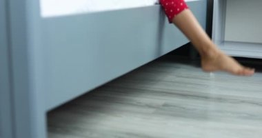 Close up Legs of a little girl , child getting out of bed in the morning after wakes up, go on the parquet or laminate floor