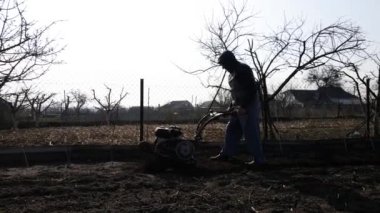 Aerial drone view Man Farmer working in the garden plows with Garden Tiller. Garden tiller, cultivator to work. Man with tractor cultivating field at spring. Modern farming, technology agriculture.