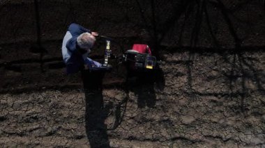 Aerial drone view Man Farmer working in the garden plows with Garden Tiller. Garden tiller, cultivator to work. Man with tractor cultivating field at spring. Modern farming, technology agriculture.