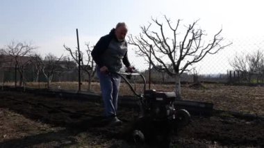 Man Farmer working in the garden plows with Garden Tiller. Garden tiller, cultivator to work. Man with tractor cultivating field at spring. Modern farming, technology agriculture.