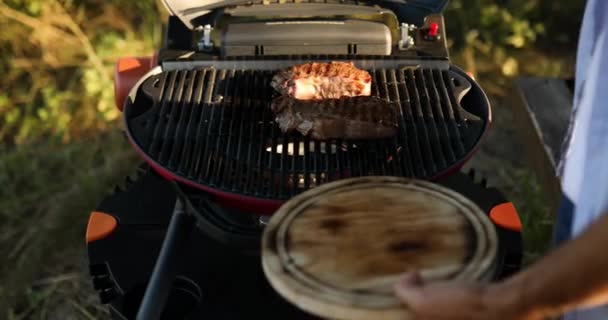 男人躺在木板上 准备吃烤牛排肉 男人在煤气炉上烤牛排 户外烧烤 夏季家庭野餐 大自然的食物 — 图库视频影像