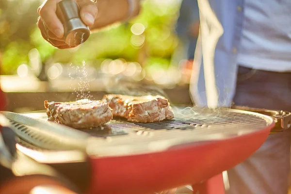 裏庭のバーベキューグリル屋外でのガスグリルで男の手の調味料の肉を閉じる 焼きローストステーキ肉 夏の家族のピクニック 自然食品 — ストック写真