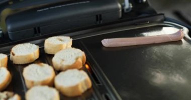 Close up on man's hand roasting bruschetta and sausages on the barbecue gas grill outdoor in the backyard, Breakfast On Grill, summer family picnic, food on the nature.