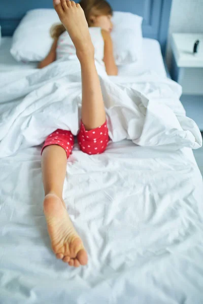 Girl\'s feet covered with white bed sheet, sleeping in a comfortable bed, Focus on the foot, healthy sleep of children