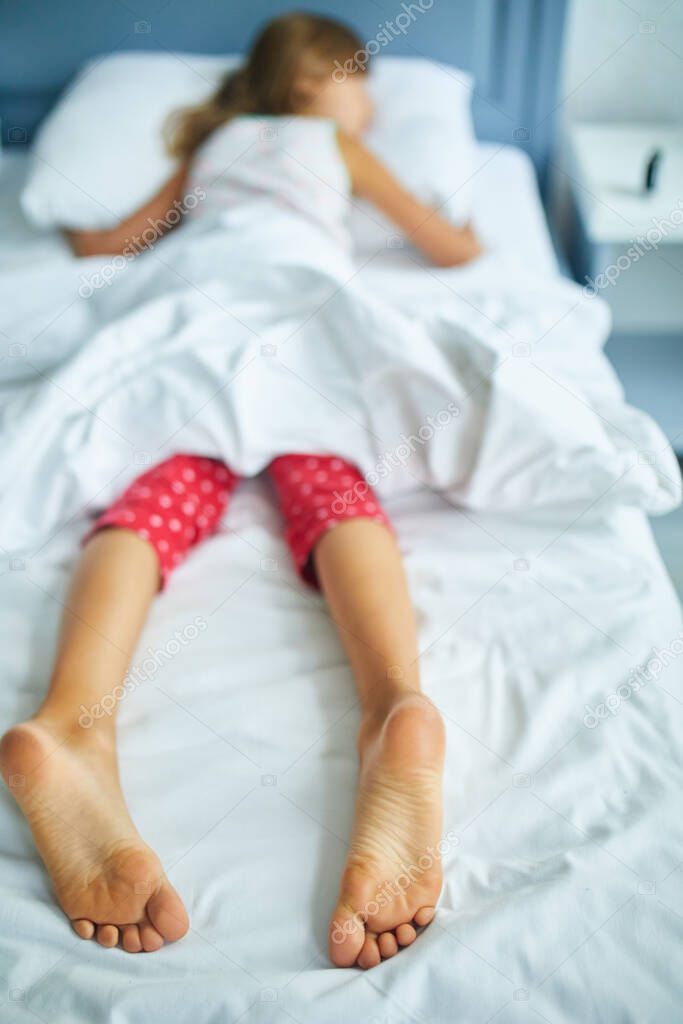 Girl's feet covered with white bed sheet, sleeping in a comfortable bed, Focus on the foot, healthy sleep of children