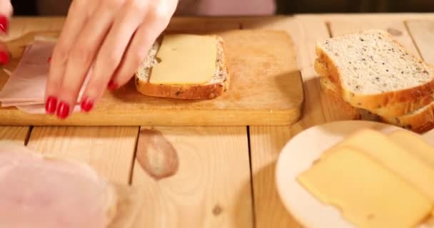 Mujer anónima haciendo Delicioso sándwich con queso y jamón sobre mesa de madera — Vídeos de Stock