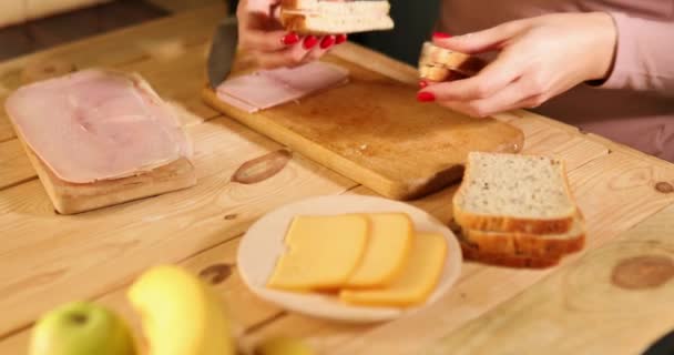 Mujer anónima haciendo Delicioso sándwich con queso y jamón sobre mesa de madera — Vídeos de Stock