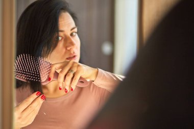 Saç dökülmesi konsepti, saç fırçasında saç dökülmesi, güzel esmer kadının sabah aynanın önünde tarakla saç taraması, güneş ışığı.,