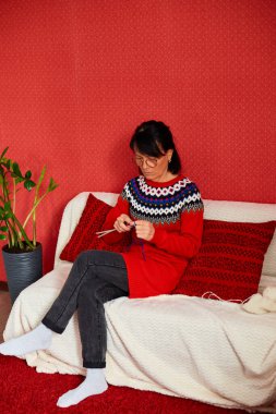 Olgun bir kadın rahat bir kanepede oturup örgü örerken hafta sonunun tadını çıkarıyor, kıdemli kadın örgü örüyor, evde dinleniyor hafta sonları en sevdiği hobi aktivitelerini yapıyor, refah kavramını geliştiriyor.