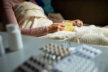 Hasta kadın elinde sıcak deniz dikenli çay kupasıyla evde battaniyenin altında oturuyor..