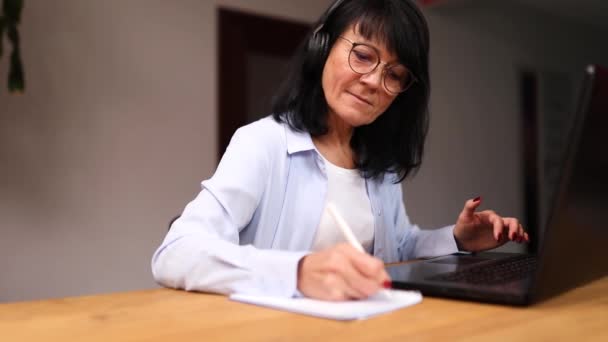 Donna matura freelance in occhiali tenendo riunione tramite videochiamata da casa — Video Stock