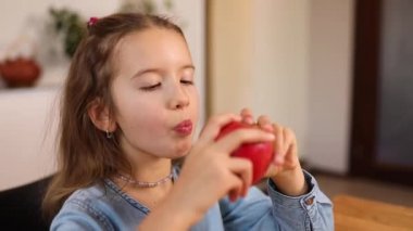 Şirin küçük kız mutfakta kırmızı elma yiyor, yavaş çekim lezzetli, mutlu çocuk, sağlıklı beslenme diyeti vejetaryen yemek yaşam tarzı.