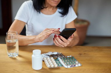 Elinde haplar ve akıllı telefonlar olan, online eczane kullanan, internetten eczane alan, internetten ilaç sipariş eden olgun bir kadın..