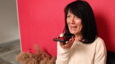 Smiling laugh mature woman record audio message on phone, female user talk speak on loudspeaker on modern smartphone, voice mail.