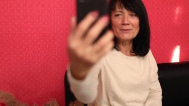 Overjoyed senior woman sit on couch at home, talk on video call on modern cell phone gadget, mature lady speak with friends using smartphone, technology concept