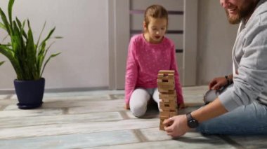 Gülümseyen küçük kız, babasıyla oynuyor. Evde ahşap bloklar inşa ediyor, eğlence ve öğrenme karıştırıyor, aile oyunu yavaş çekimde birlikte oynuyor.