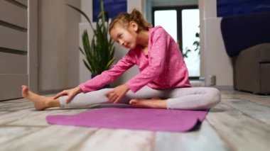 Küçük kız esneme egzersizleri yapıyor, evde fitness minderinde yoga yapıyor spor yapıyor, sağlıklı bir yaşam tarzı sergiliyor. Çocuklar ev karantinası yapıyor