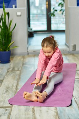 Küçük kız esneme egzersizleri yapıyor, evde fitness minderinde yoga yapıyor spor yapıyor, sağlıklı bir yaşam tarzı sergiliyor. Çocuklar ev karantinası yapıyor
