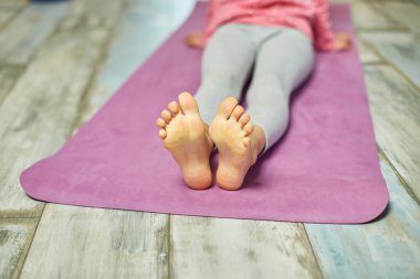 Ayaklarını kapat küçük kız esneme egzersizleri yapıyor, evde yoga yapıyor spor yapıyor, sağlıklı yaşam tarzı uyguluyor. Çocuklar ev karantinası yapıyor