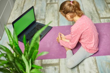 Küçük kız dizüstü bilgisayarda yeşil ekranda video izliyor ve evde esneme egzersizleri yapıyor. Kişisel antrenörle uzak çocuk eğitimi, online eğitim konsepti, spor yapmak, sağlıklı yaşam tarzı.