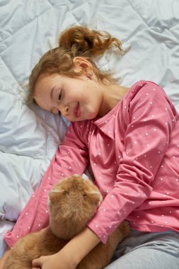 Tatlı zencefilli kedi ve küçük kız yatakta yumuşak bir battaniyeye uzanıyor, çocuk sevdalısı hayvanlar, kedi uykusu, rahat bir ev ve rahatlama konsepti, sabah yatma zamanı..