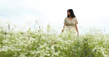 Çiçek açan çayırlarda, kırsalda yürüyen elbiseli bir kadın.