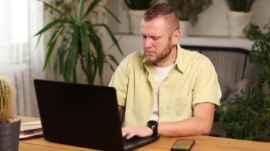 Evde dizüstü bilgisayarla çalışan serbest çalışan bir adam. Uzaktan kumanda için bilgisayarda yazan bir erkek.