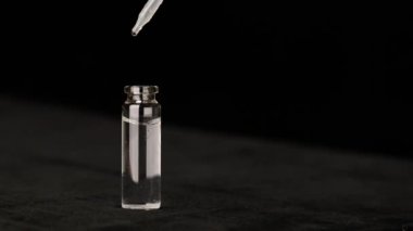 Siyah arka planda gözlük şişesinden bir damla su, doğal malzemelere dayanan kozmetik yağları.