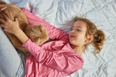 Tatlı zencefilli kedi ve küçük kız yatakta yumuşak bir battaniyeye uzanıyor, çocuk sevdalısı hayvanlar, kedi uykusu, rahat bir ev ve rahatlama konsepti, sabah yatma zamanı..