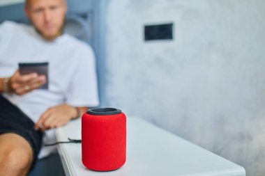 Erkek testi, akıllı telsiz hoparlörü, ses komutlarıyla ev aletlerini kontrol eden adam, evdeki kanepede oturmak, akıllı ev kavramı.