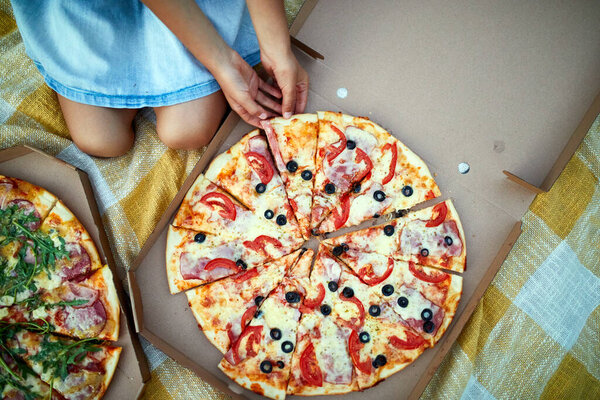 Sharing pizza, little girl hands taking a piece of pizza from a box outdoor, family picnic, eating pizzas for dinner, fast food delivery.