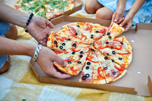 Sharing pizza, hands taking a piece of pizza from a box outdoor, family picnic, eating pizzas for dinner, fast food delivery.