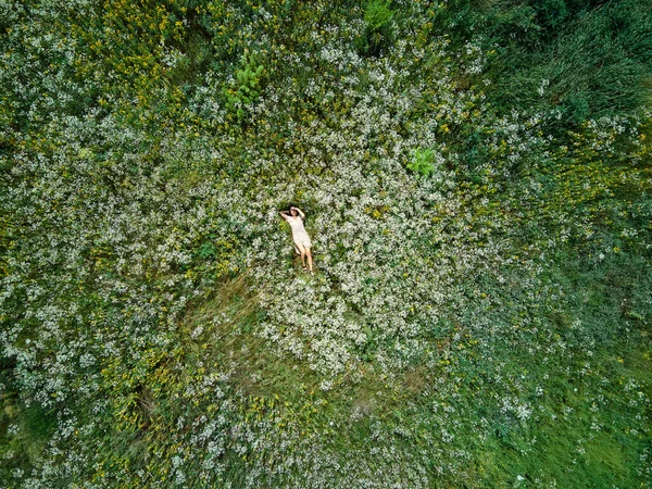 Drone aerial view of relax woman in dress lying on flower blooming meadow, in countryside, in the field on summer day, feel the nature, alone travel. Slow motion, top view.