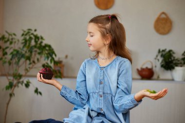 Küçük kız yiyecekleri karşılaştırıyor, mikroyeşil keki mikro-yeşil kötü alışkanlığa tercih ediyor, yetersiz beslenme kavramı.