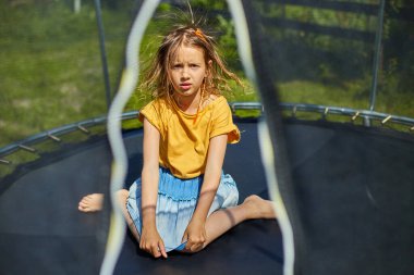 Trambolinde elektrikli saçları olan genç bir kızın portresi evin arka bahçesinde güneşli bir yaz günü, yaz tatili, trambolinde zıplayan mutlu küçük bir çocuk.