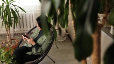 Telefon kullanan, akıllı telefon uygulamalarını tarayan, ekrana bakan, kadın, internet mağazasından alışveriş yapan ev bahçesindeki koltukta oturan, biyofili tasarımı.