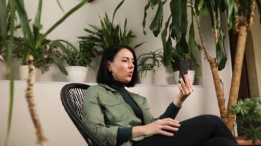 Modern cep telefonu cihazında gülümseyen mutlu kadın konuşması. Arkadaşlarıyla uzaktan konuşma, bayan ailesiyle akıllı telefon kullanma, teknoloji konsepti ev bahçesindeki kanepede oturma, biyofili tasarımı..