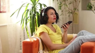 Hedphone 'lu bir kadın, kanepeye uzanır, akıllı telefonda sanal komut asistanı, sesli çeviri uygulaması reklam konsepti, yeni teknoloji konsepti, cihazdaki dijital ses asistanını çalıştırır.