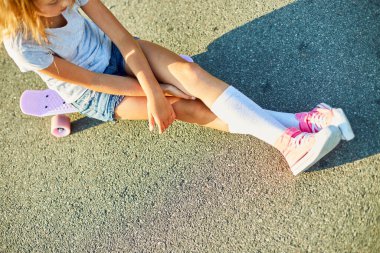 Kaykay kullanmayı öğrenen küçük bir kız, beyaz çoraplar ve pembe ayakkabılar giyen isimsiz bir çocuk yaz şehrinin kırsal kesiminde kaykaya biniyor..