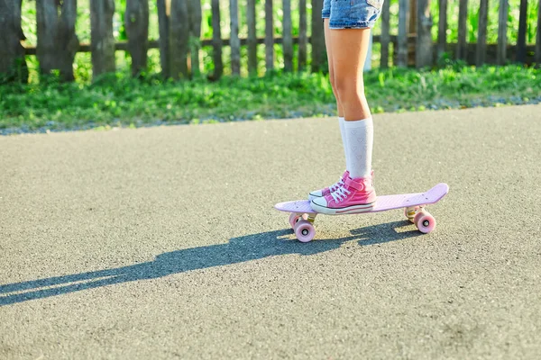 スケートボードを使うことを学ぶ小さな女の子 白い靴下とピンクの靴を着た匿名の子供夏の街の田舎道でスケートボードに乗る — ストック写真