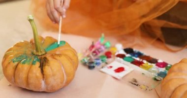 Evde balkabağı süsleyen mutlu çocuk. Küçük kız, turuncu Cadılar Bayramı 'nda balkabağı Jack-O-Lantern' in yüzünü çiziyor. Tatil dekorasyonu kavramı